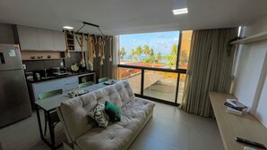 A compact living space with a kitchenette, a sofa, and a view of a tropical landscape.