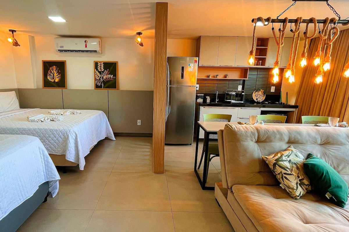 A compact hotel room with two beds, a sofa, a kitchenette, and a dining area.