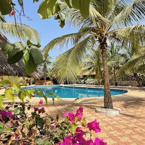 A swimming pool surrounded by palm trees and a thatched-roof structure.