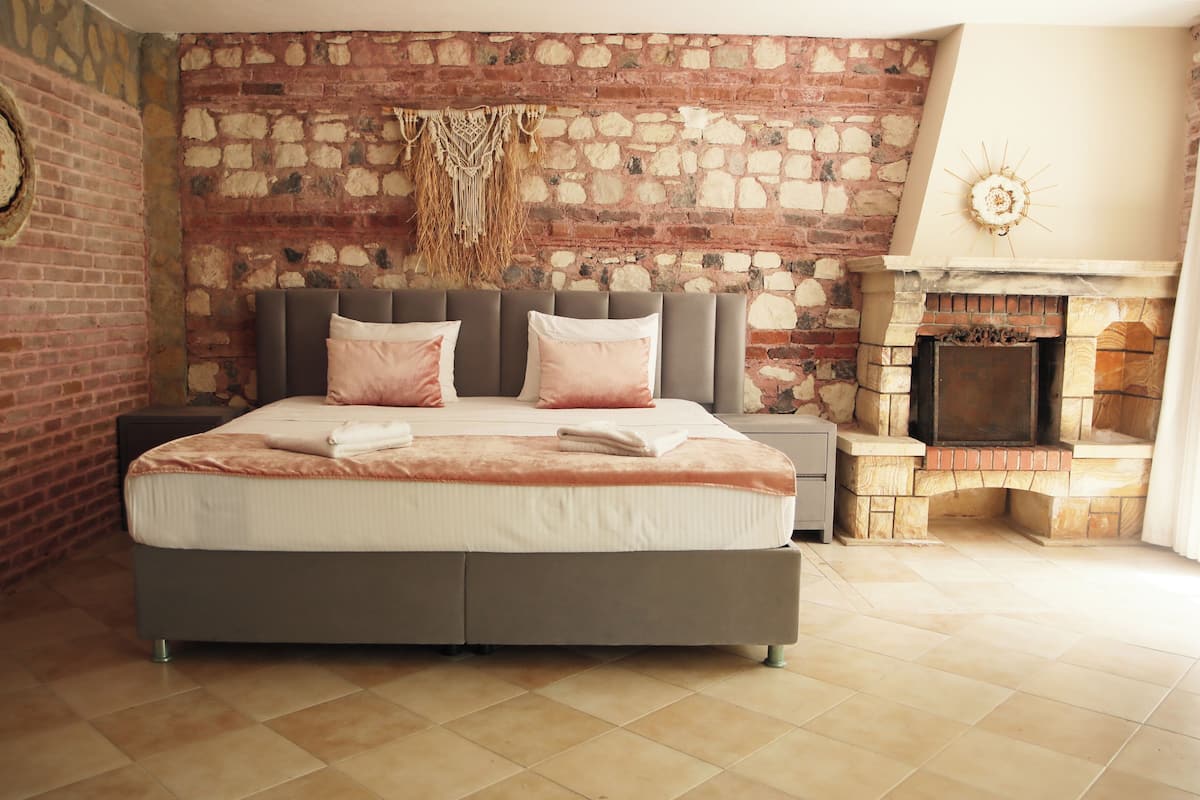 Un dormitorio con pared de piedra, una cama con almohadas, una mesita de noche y una chimenea.