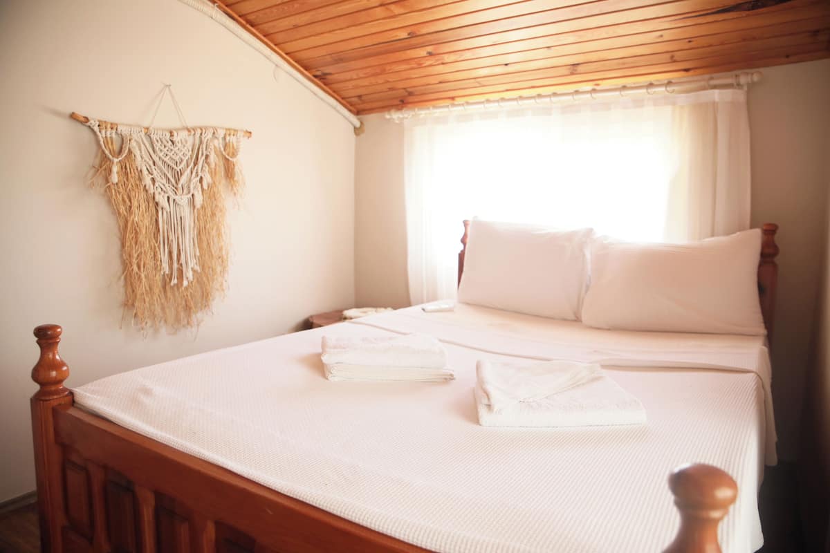 Una cama bien hecha con sábanas y almohadas blancas, un cabecero de madera y un tapiz de nudos colgando de la pared.