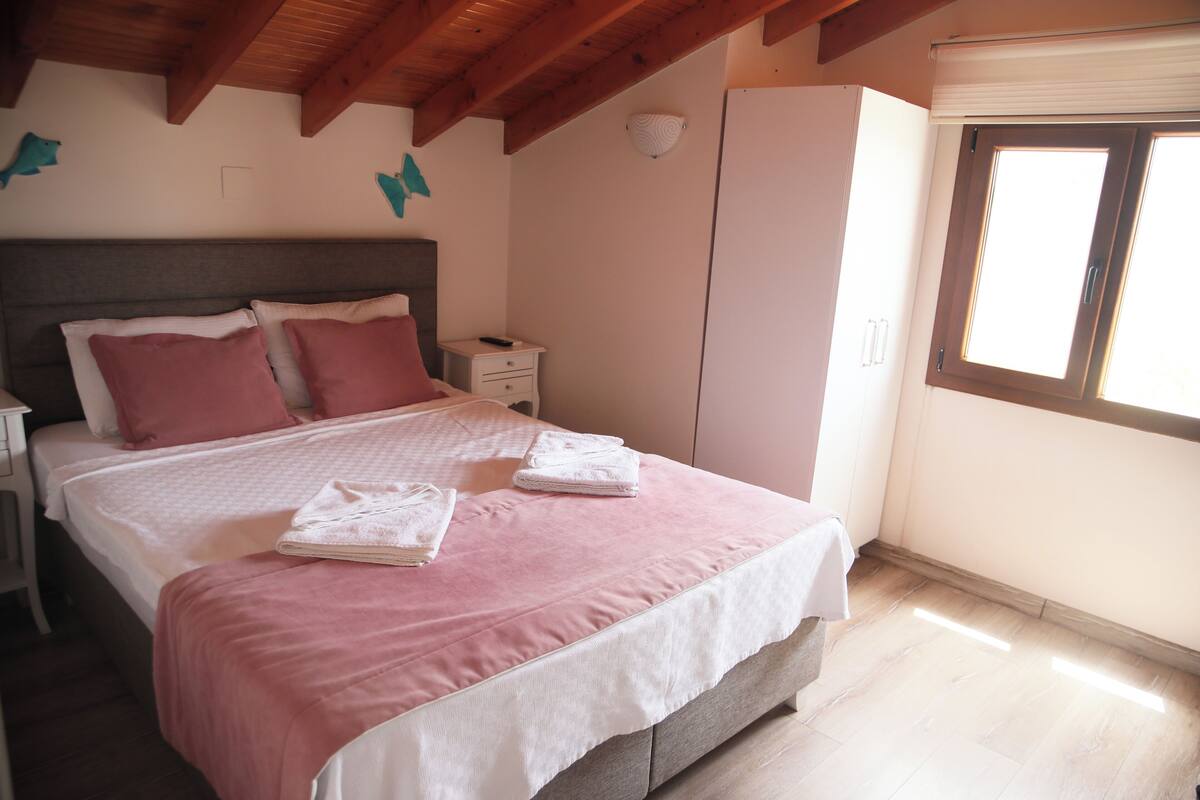 Un dormitorio con cama, almohadas, una mesita de noche, un armario y una ventana.