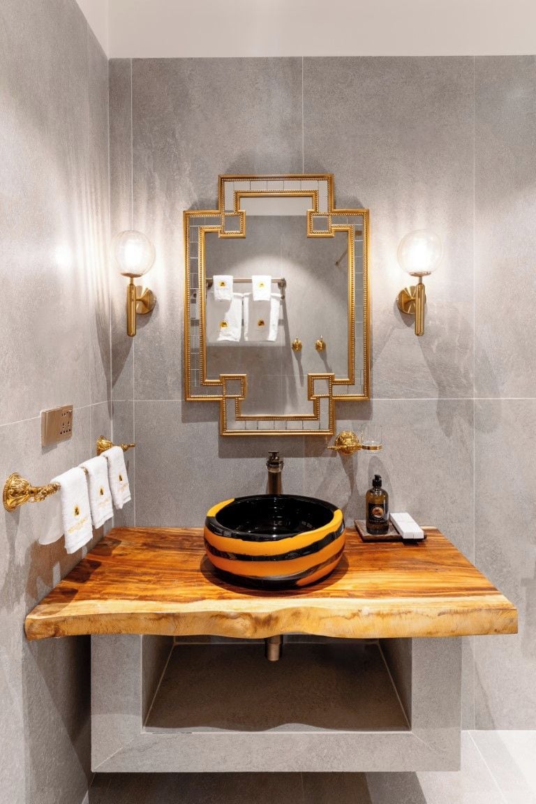 A bathroom with a wooden vanity, a round sink, a gold-framed mirror, and two wall-mounted lights.