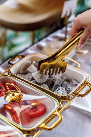 A tray with food items including dragon fruit and watermelon, held by a golden-handled fork.
