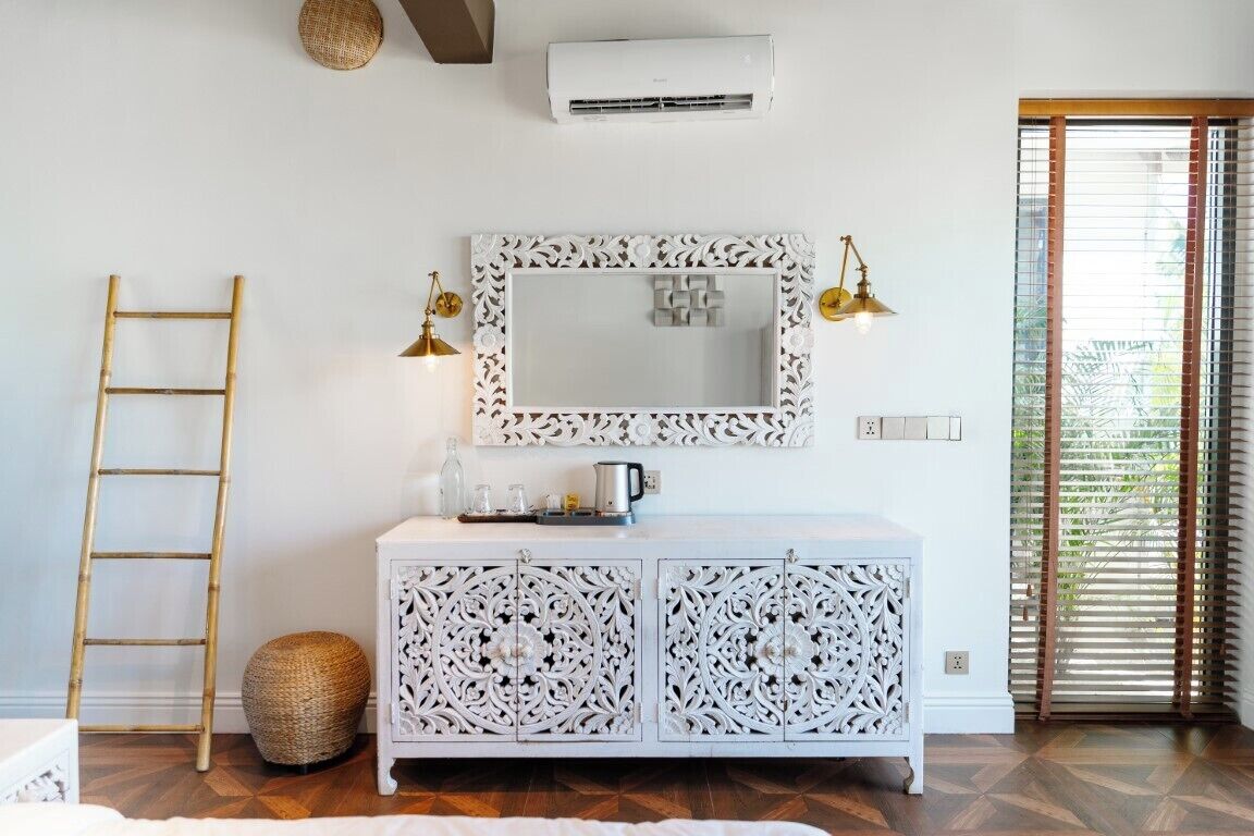 A room with a white cabinet, a mirror with ornate frame, a ladder, and a basket.
