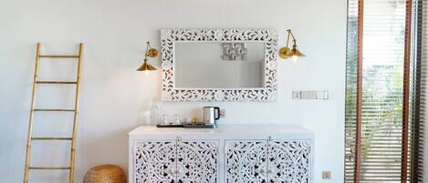 A room with a white cabinet, a mirror with ornate frame, a ladder, and a basket.