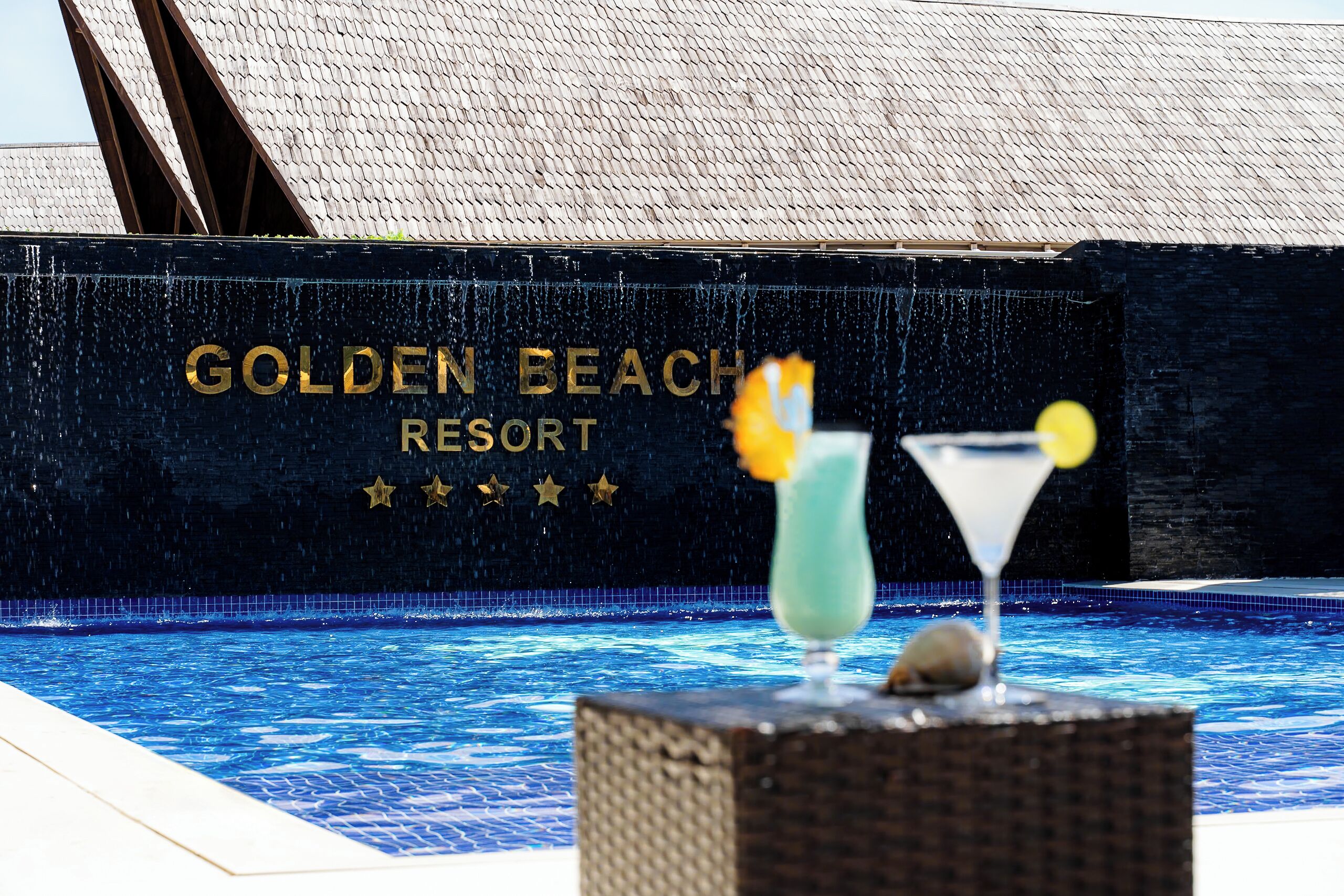 A pool area at Golden Beach Resort with a sign in the background and a cocktail on a table.