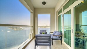 A balcony with a view of the sea and cityscape, a table with chairs, and a glass door leading to a room.