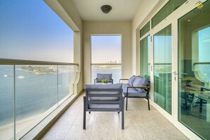 A balcony with a view of the sea and cityscape, a table with chairs, and a glass door leading to a room. - Palm Jumeirah Apt w/ Beach Access & Sea View (Dubai)