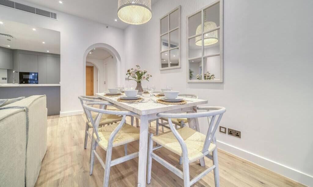 A dining area with a white table set for four, surrounded by white chairs with woven seats.