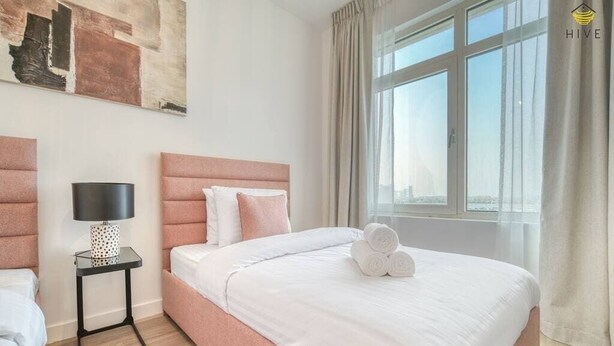 A modern hotel room with a large bed, a bedside table with a lamp, and a view of the city through large windows.