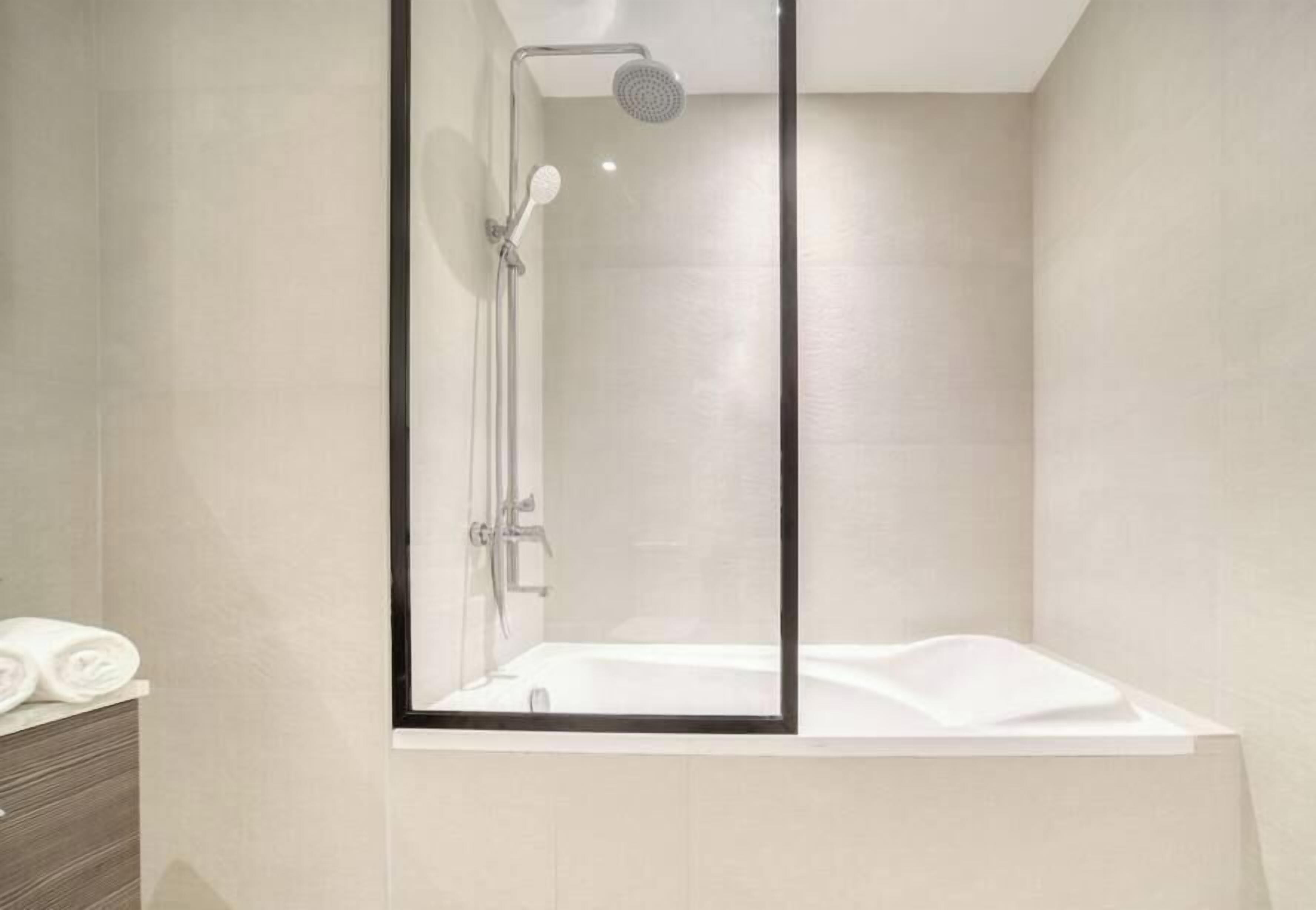 A modern bathroom with a glass-enclosed shower, a white bathtub, and a wooden cabinet.