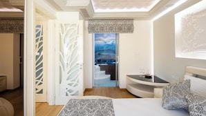 A modern bedroom with a large bed, a small table with glasses, and a view of a kitchen and stairs. - DeMaNi President Suites (Sitia)
