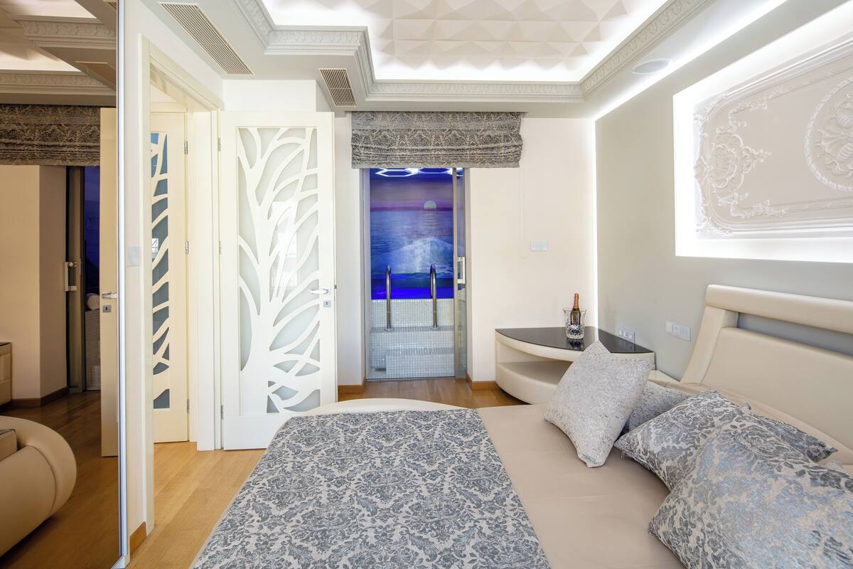 A modern bedroom with a large bed, a nightstand, and a bathroom visible through a glass door.