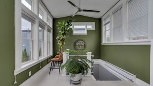 Une pièce dotée d’un ventilateur de plafond, de grandes fenêtres, d’une plante en pot, d’un coin repas avec des chaises et d’une baignoire.