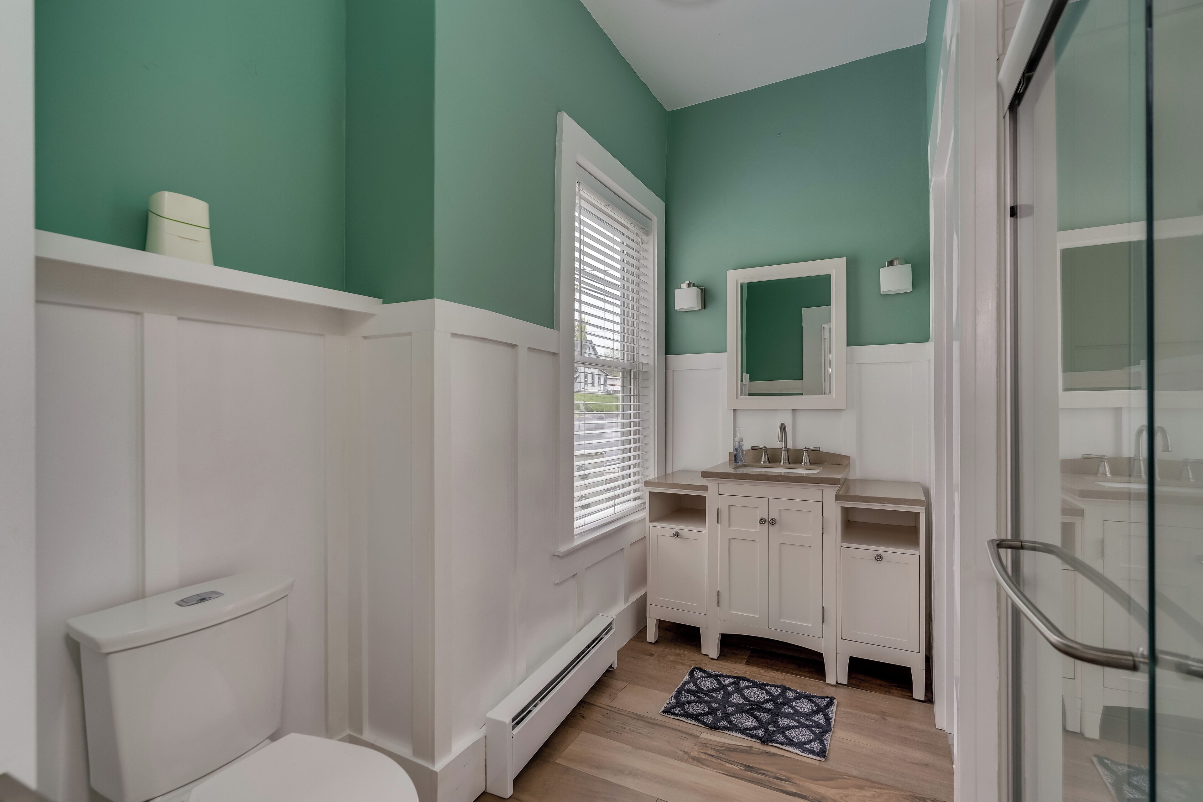 A bathroom with a toilet, vanity, and a window with blinds.