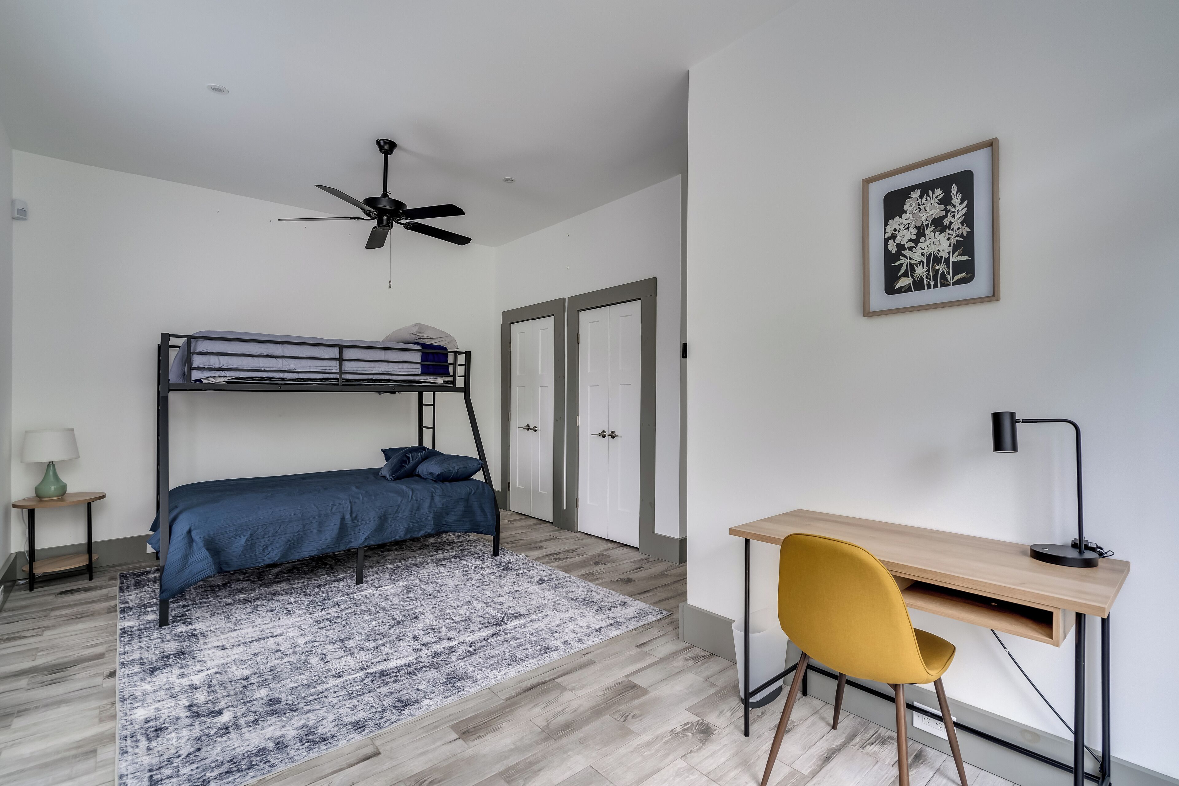Makuuhuoneessa on kerrossänky, työpöytä tuolilla, kattotuuletin ja seinällä oleva kehystetty kuva.