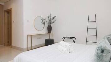 A hotel room with a bed, a bedside table with a vase, a mirror, and a ladder against the wall.