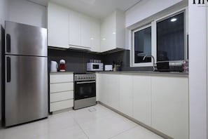 Una cocina moderna con gabinetes blancos, un refrigerador de acero inoxidable, un microondas y un horno.