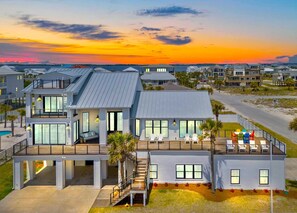 A modern two-story house with a large deck, a swimming pool, and a view of the ocean at sunset. - 20ft Beach Access, Sleeps 31, Pool, Bikes, Basketball,Ping Pong,2 Kitchens, Pets (Pensacola Beach)