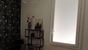 Ein Schlafzimmer mit einem Bett, einem Fenster mit Jalousien, einer Ablage mit Dekoration und einer Wand mit Blumenmuster.