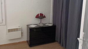 Ein Eckzimmer mit einem schwarzen Schminktisch, einem roten Fächer und einem weißen Lüftungsgitter.