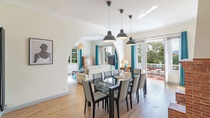 A modern dining area with a glass table and chairs, a TV mounted on the wall, and a view of the outdoors through large windows. - Haut de Villa 6 Personnes Juan les Pins Résidentiel Proche Plage (Antibes)