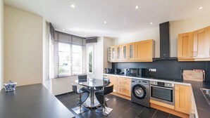 A modern kitchen with a dining area, featuring a washing machine, microwave, and wooden cabinets. - Haut de Villa 6 Personnes Juan les Pins Résidentiel Proche Plage (Antibes)