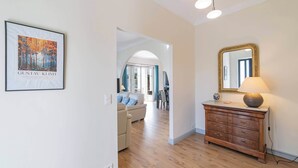 A well-lit hallway with a framed artwork, a wooden dresser with a lamp, and a dining area in the background. - Haut de Villa 6 Personnes Juan les Pins Résidentiel Proche Plage (Antibes)