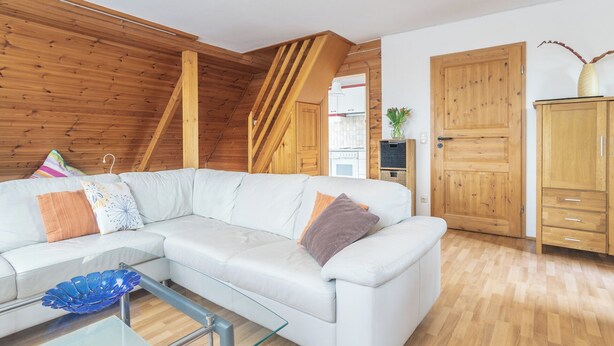 A modern living room with a white sofa, glass coffee table, wooden ceiling beams, and a wooden cabinet. - Alpen-hostel Südgrat 8, Buxacher Straße 23 mit Motorradvermietung (Memmingen)