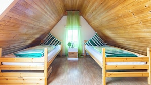 A cozy attic bedroom with two wooden bunk beds, a small bedside table, and a window with green curtains. - Alpen-hostel Südgrat 8, Buxacher Straße 23 mit Motorradvermietung (Memmingen)
