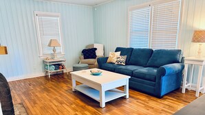 Een woonkamer met een blauwe bank, een witte salontafel en houten vloeren.
