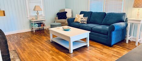 A living room with a blue sofa, white coffee table, and wooden flooring.