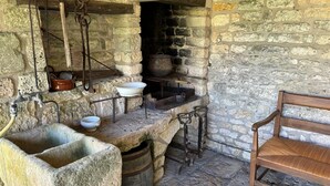 Une cuisine rustique en pierre, avec un banc en bois, des éviers en pierre et un grand pot sur la cuisinière.