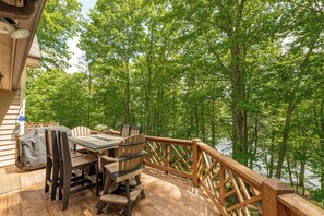 A wooden deck with a table and chairs, overlooking a forested area and a body of water. - New! Cozy Lakefront Retreat w/ Scenic Views (McHenry)