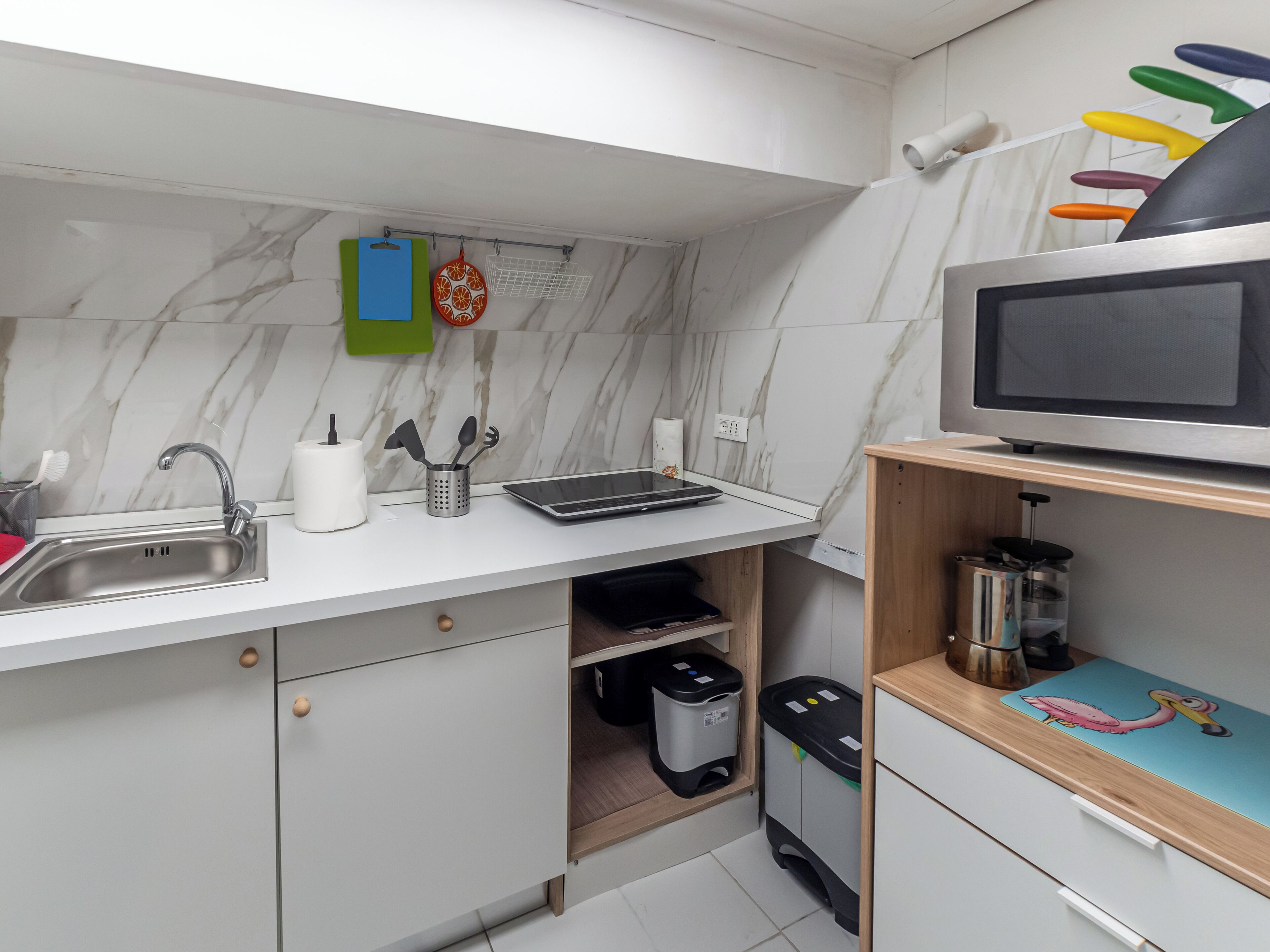 A modern kitchen with a marble backsplash, stainless steel sink, and a flat-screen TV on a wooden shelf.