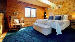 A cozy log cabin bedroom with a large bed, a small table, and a chair. - Spacious Spring Lake Retreat • Beach Access • Sleeps 8 • Family & Pet Friendly (Spring Lake)