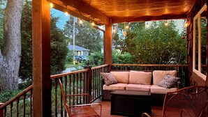 A wooden deck with a cushioned seating area, two wicker chairs, and a view of a house and trees. - Spacious Spring Lake Retreat • Beach Access • Sleeps 8 • Family & Pet Friendly (Spring Lake)