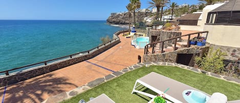 Una propiedad costera con piscina, sillas de descanso y vista al océano.