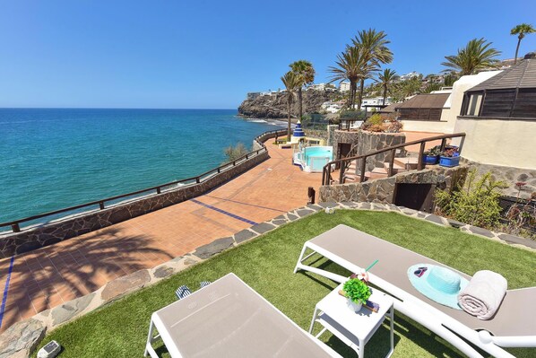 Una propiedad costera con piscina, sillas de descanso y vista al océano.
