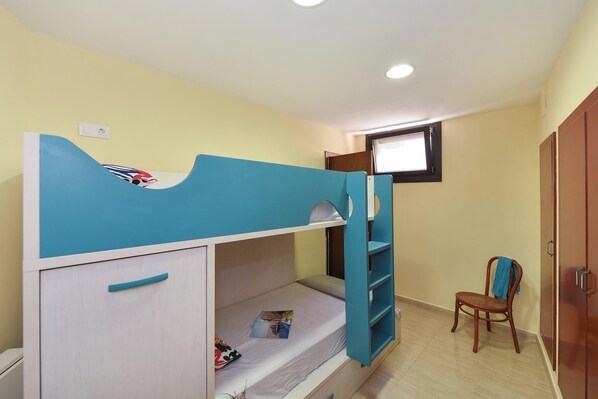 Un lit superposé avec un bureau et une chaise, une fenêtre et une armoire, dans une pièce aux murs de couleur claire.