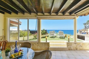 Une terrasse couverte avec une table dressée pour les repas, une vue sur la mer et des sièges d’extérieur.