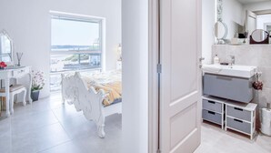 Un dormitorio moderno con un ventanal grande, una cama con cabecero decorado, un tocador con espejo y vistas al mar.