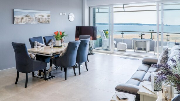 Una sala de estar moderna con comedor, ventanas amplias y vista a la playa.