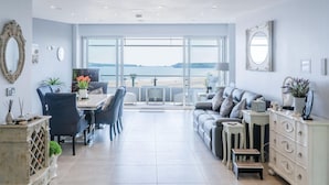 Amplia sala de estar con vista al mar, comedor con mesa y sillas, y zona de estar con sofá y cojines.