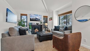 A modern living room with a fireplace, grey sofas, a brown leather chair, and artwork on the walls. - Hidden Creek by Park City Vacations (Park City)