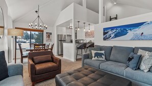 A spacious living area with a grey sofa, brown armchair, and ottoman, a dining table with chairs, and a kitchen in the background. - Hidden Creek by Park City Vacations (Park City)