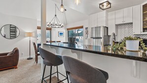 A modern kitchen with white cabinets, a stainless steel refrigerator, and a large island with bar stools. - Hidden Creek by Park City Vacations (Park City)