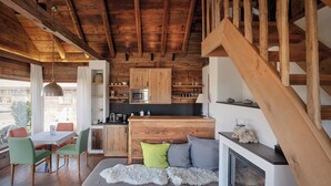 A rustic cabin interior with a wooden dining area, a kitchen with wooden cabinets and a microwave, a cozy seating area with cushions, and a fireplace.