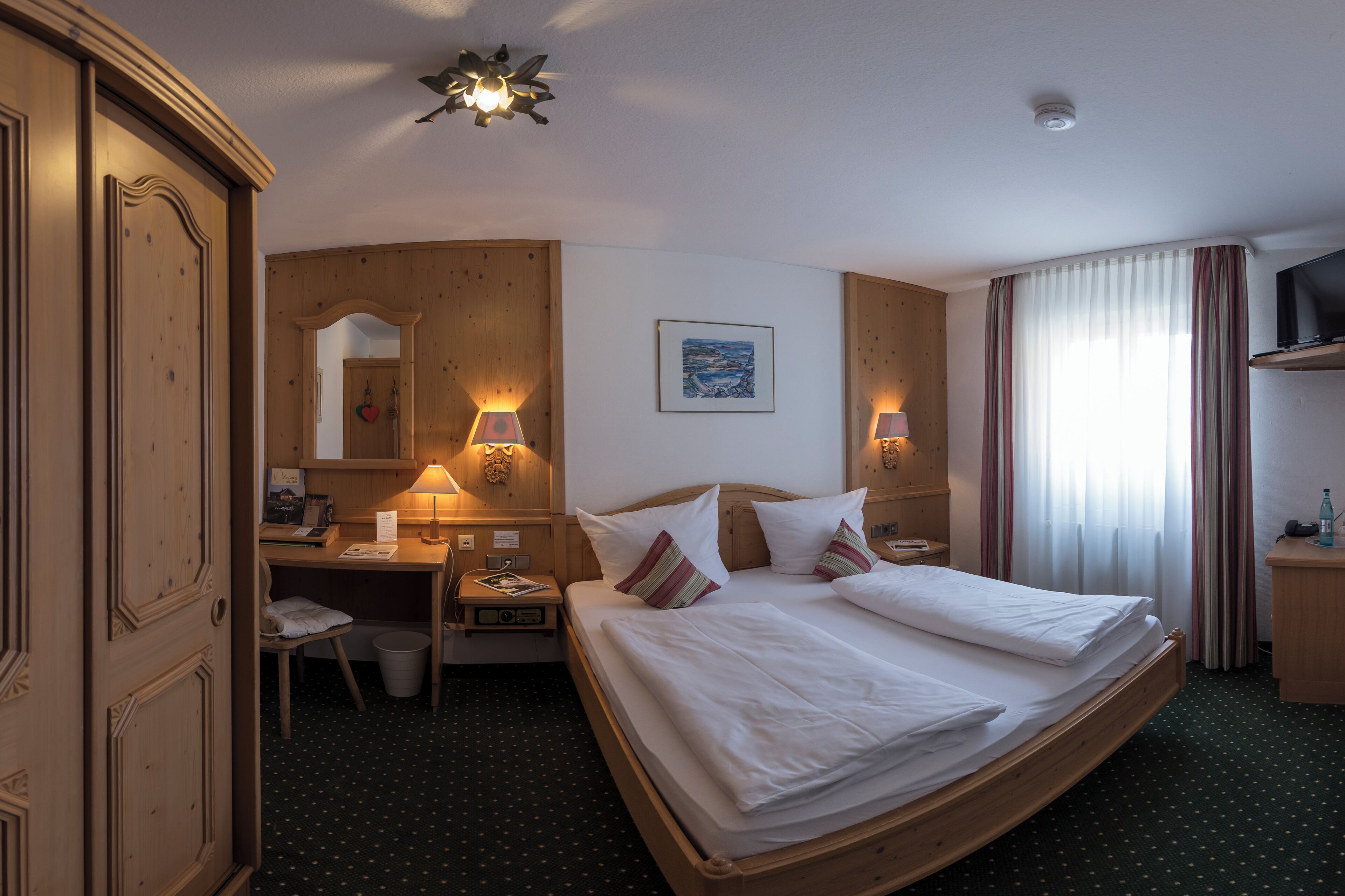 A hotel room with a large bed, a desk with a chair, a television, and a mirror on the wall.